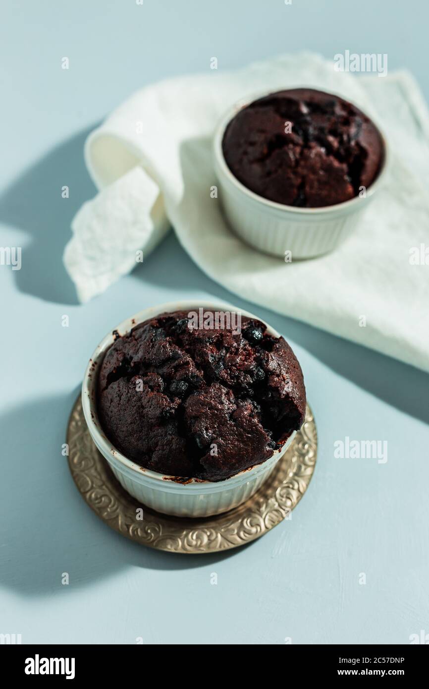Hausgemachte Schokoladen-Rote-Bete-Muffins mit Heidelbeeren in weißen Kuchendosen auf blauem Hintergrund, weiße Serviette, Hart-Light-Shot Stockfoto