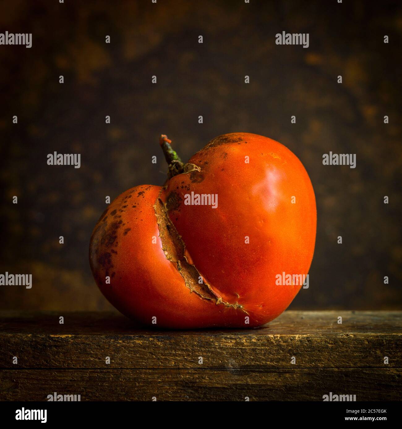 Beschädigte rote Tomate auf braunem Hintergrund isoliert Stockfoto