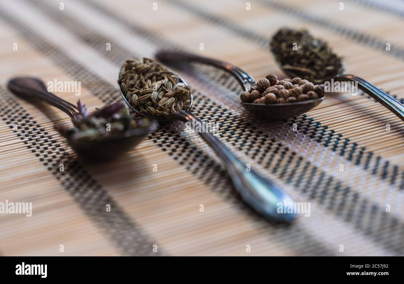Vier Löffel mit aromatischen Kräutern zum Würzen der Speisen auf einem Holzteppich Stockfoto