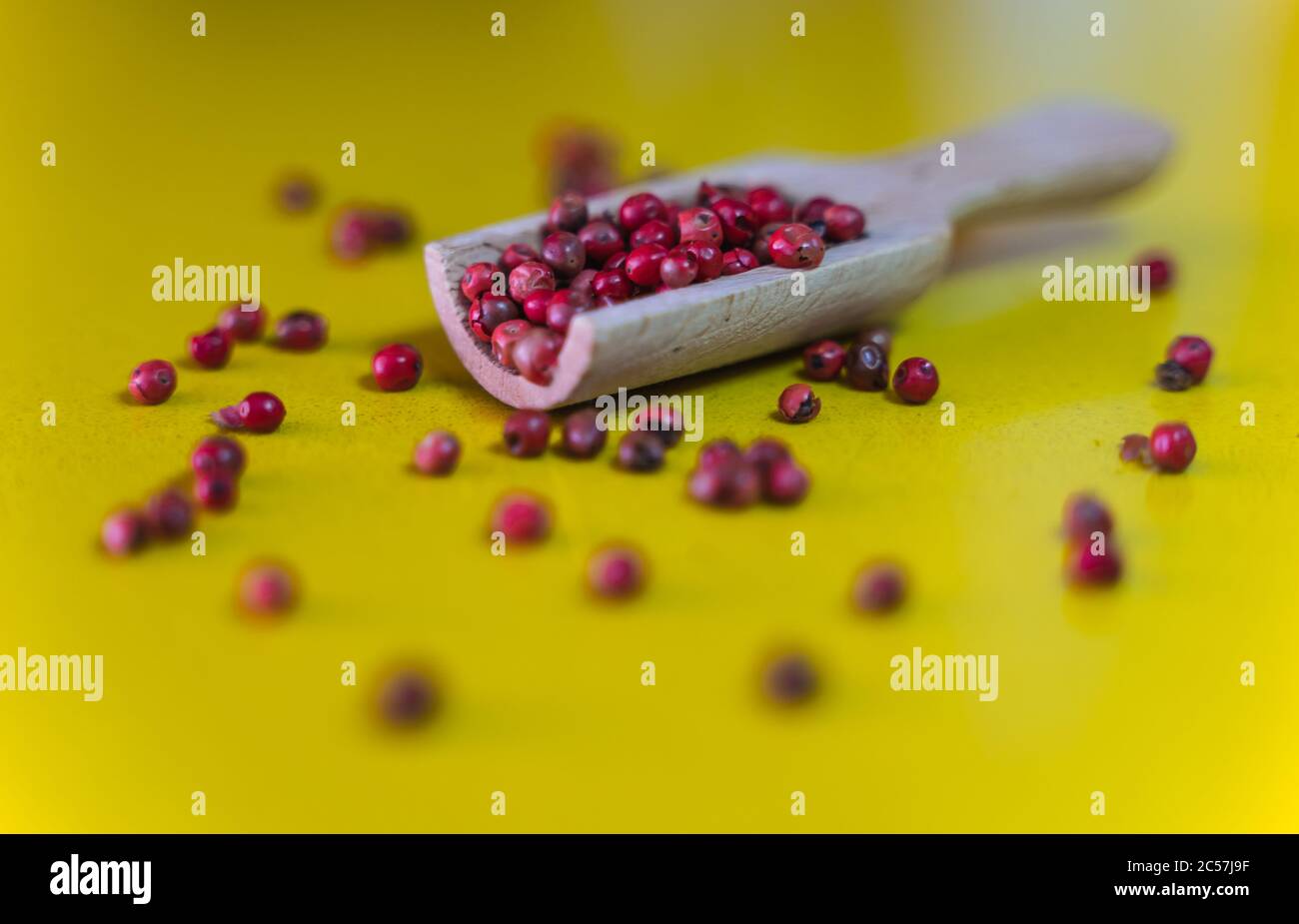 Studiofoto eines Holzlöffels mit roten Beeren auf gelber Oberfläche und Hintergrund Stockfoto