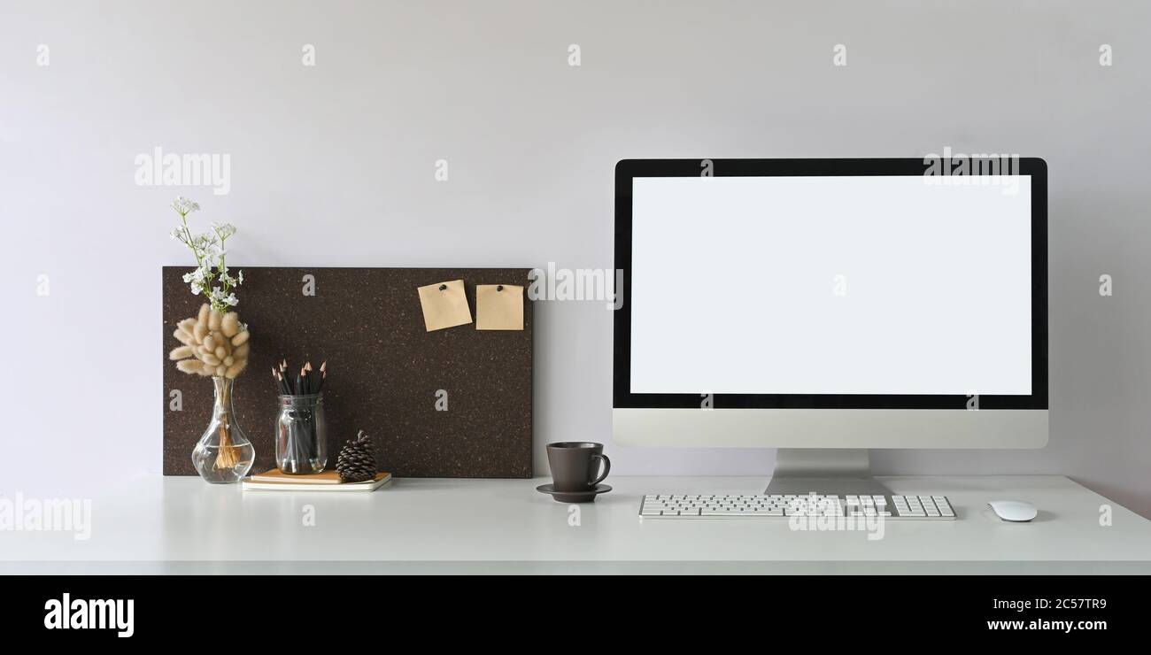 Ein weißer Schreibtisch ist von einem weißen Bildschirm mit Computermonitor und Büroausstattung umgeben. Stockfoto