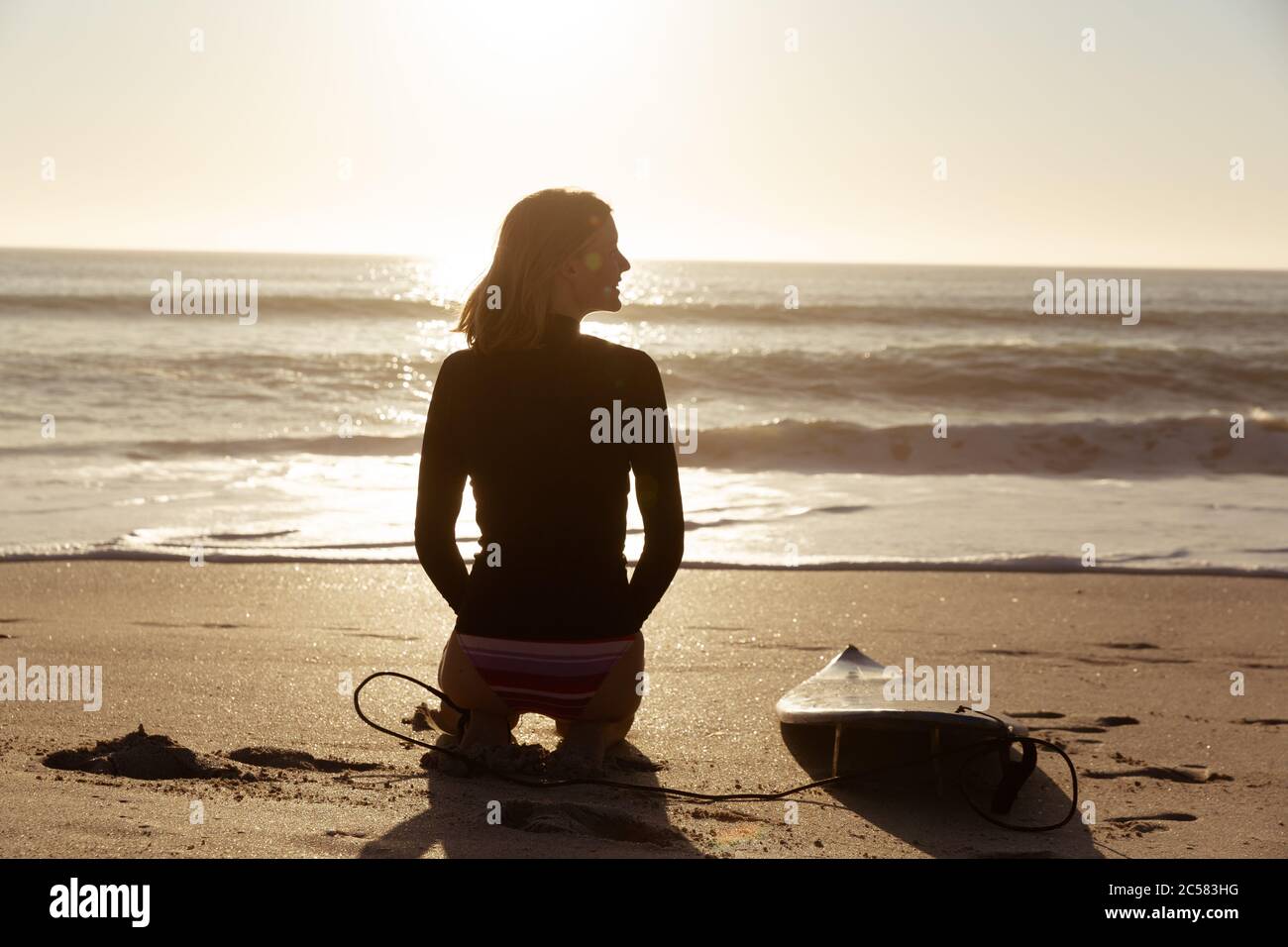 Frau mit Surfbrett am Strand zu sitzen Stockfoto