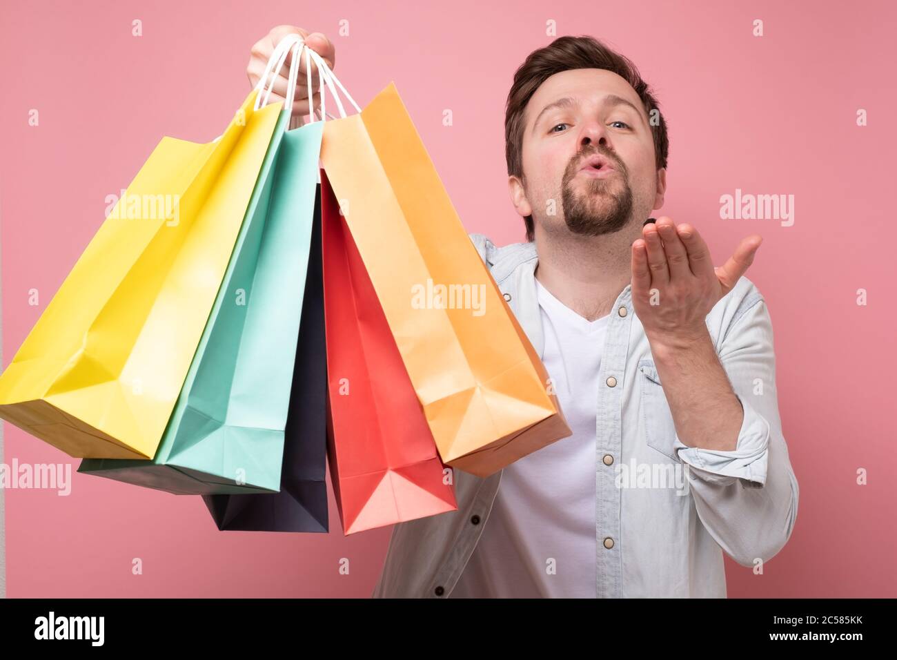 Junger Kaukasianer hält Einkaufstasche und sendet Luftkuss. Stockfoto