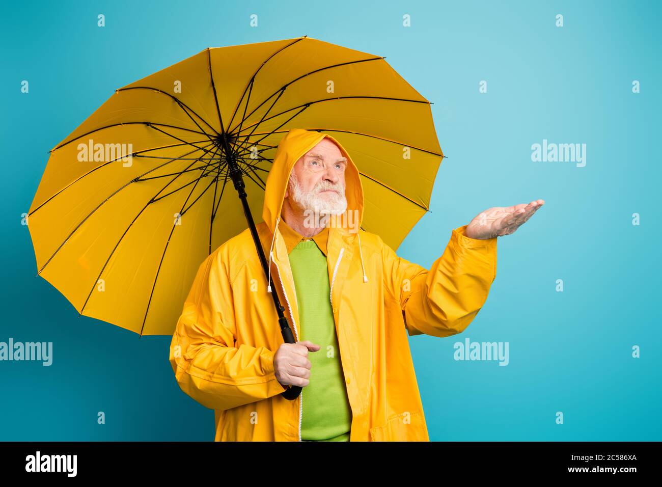 Porträt seines er unzufrieden grauhaarigen Mann trägt gelben Mantel hält regnerischen Tropfen auf der Handfläche warten Erwartung Prognoseänderung isoliert über Stockfoto