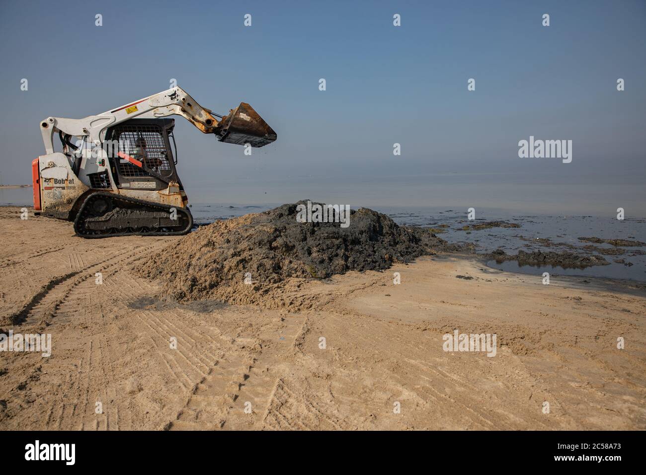 Skid Steer Lader oder Bobcat, arbeitet, um den Strand zu reinigen Stockfoto