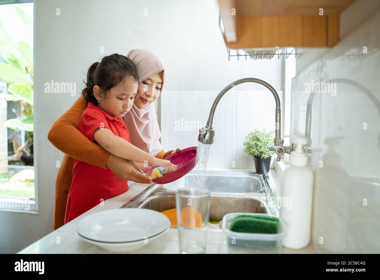 Helfende Hand. Nettes kleines Mädchen Helfen Sie ihr muslimische Mutter in Waschen Geschirr bei Familie Küche Stockfoto