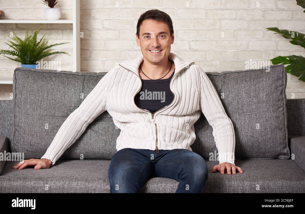Glücklicher Mann in einem weißen Pullover sitzt auf einem Sofa zu Hause Stockfoto
