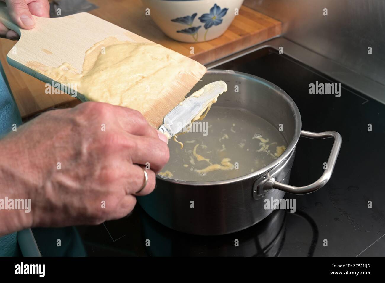 Kochen spätzle, Hände eines Mannes kratzen hausgemachten Eiernudelteig von einem Holzbrett in kochendes Wasser, typisches Gericht in Schwaben, Südland Stockfoto