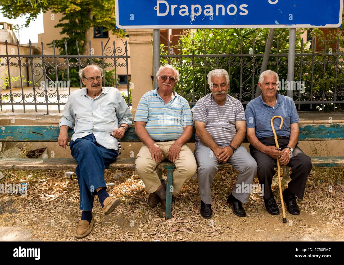 Vier griechischen Männer sitzen auf einer Bank durch die Dorfkirche in Kefalas in Kreta unter ein Schild zu Drapanos und Kokkino Chorio Stockfoto