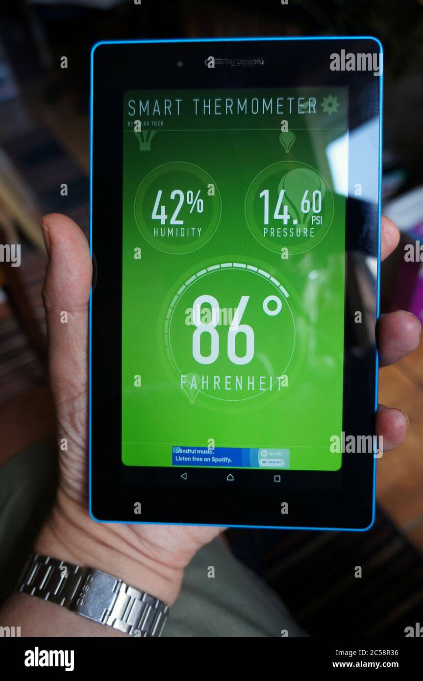 Hand mit einem Tablet-PC, der die aktuelle Temperatur und Luftfeuchtigkeit von 86F °c in der Wetter-App anzeigt Stockfoto