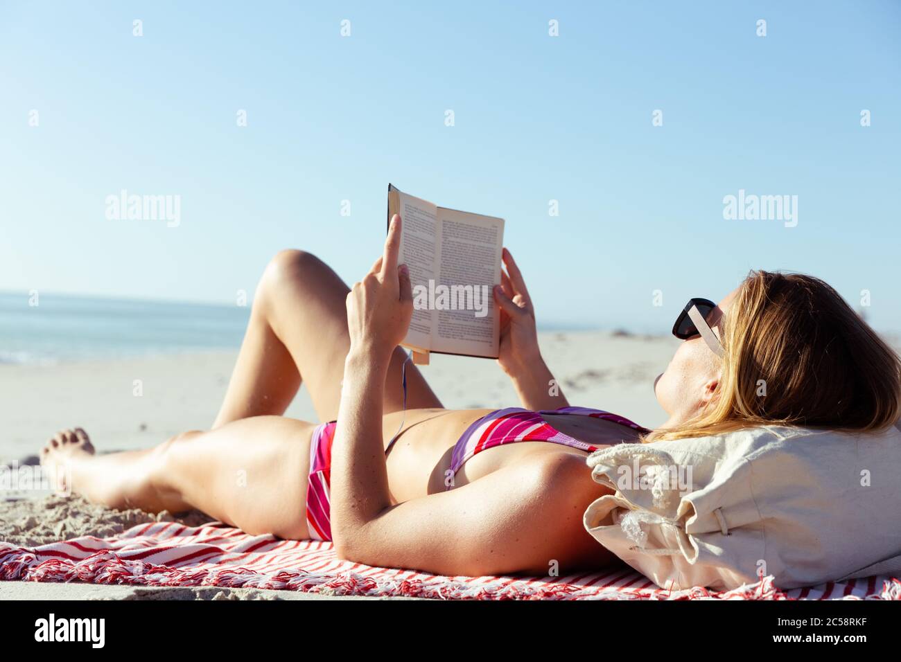 Frau liest ein Buch, während sie am Strand liegt Stockfoto