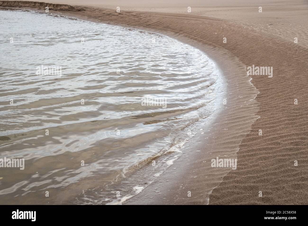 Kleine, hell schimmernde Wellen, die gegen die geschwungene Wobel eines sandigen Strands, St Andrews, Schottland, schlagen Stockfoto