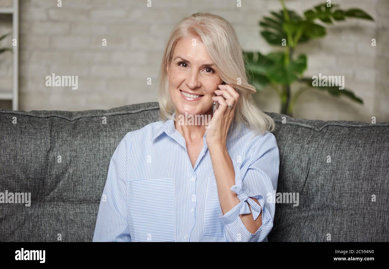 Glückliche 50 Jahre alte Frau spricht zu Hause am Telefon Stockfoto