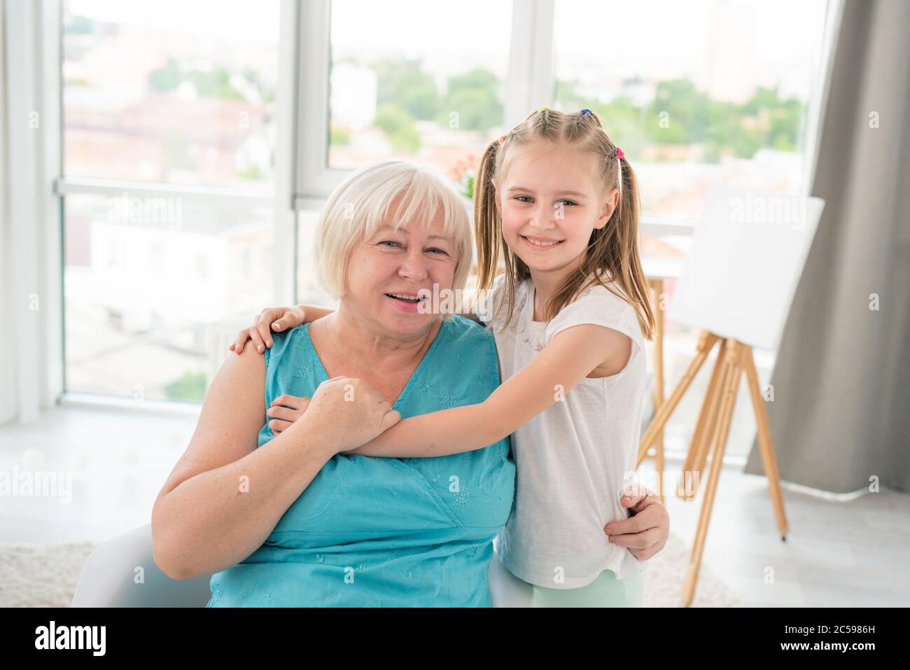 Nettes kleines Mädchen umarmt lächelnd Oma im hellen Raum Stockfoto