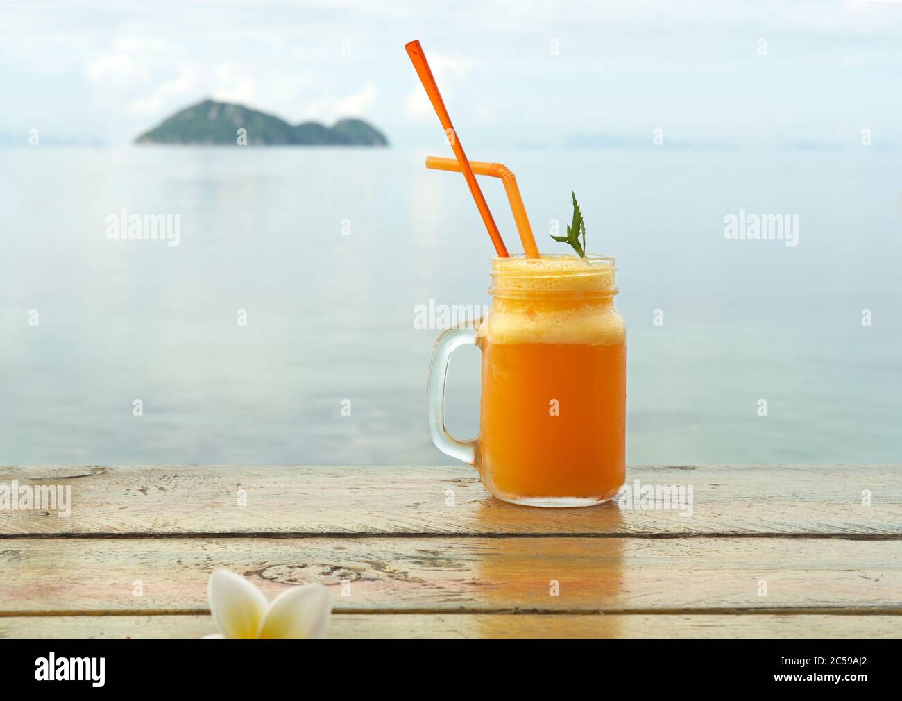 Sommercocktail mit verschiedenen tropischen Früchten. Apfel, Mandarine, Mango Mischung. Glas Orangengetränk mit verschwommenem Meer auf dem Hintergrund Stockfoto