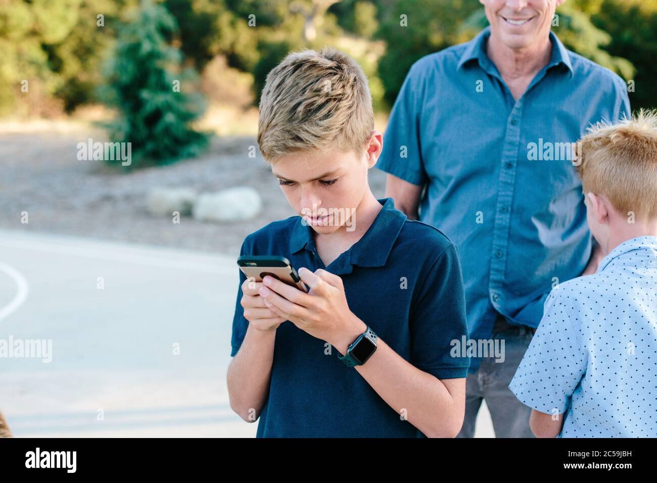 Teenager schaut sich sein Smartphone an, während er draußen mit Familie ist Stockfoto
