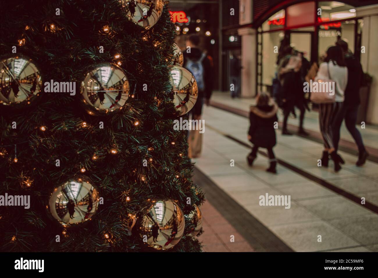 Einkäufer, die an einem Weihnachtsbaum in einem Einkaufszentrum oder Einkaufszentrum vorbeilaufen, Gunwharf Quays, Portsmouth, Großbritannien Stockfoto