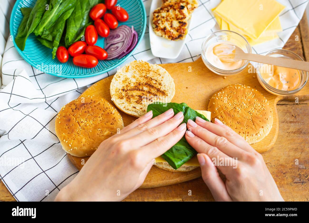 Vorbereitung aller Zutaten für die Herstellung eines Burger - Brötchen, Cutlet, Käse, Salat, Tomaten, Saucen. Die Hände des Mädchens nehmen eine Burger Rolle und legen die s Stockfoto