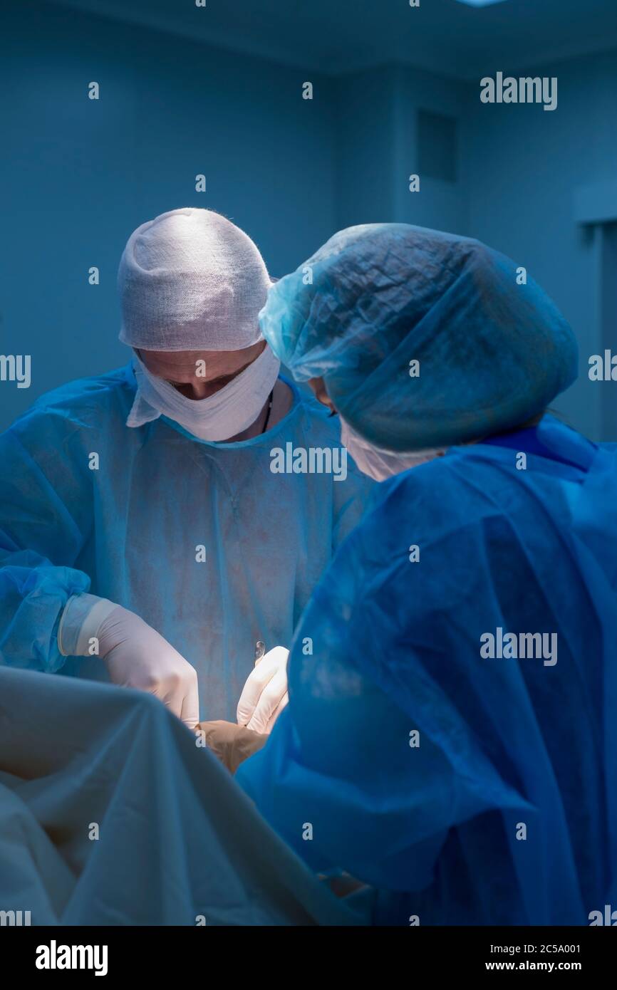 Kinderchirurgen führen urologische Operationen durch. Ein Mann und eine Frau in einer Maske und einem blauen sterilen Gewand im Operationssaal. Stockfoto