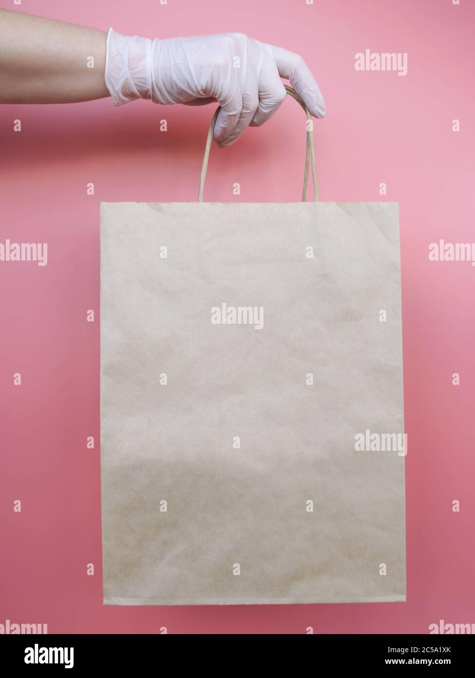 Frau, die Papiertüte hält, Hand in medizinischen Handschuh als Schutz vor Viren. Kontaktlose Lieferung während der Quarantänezeit. Stockfoto