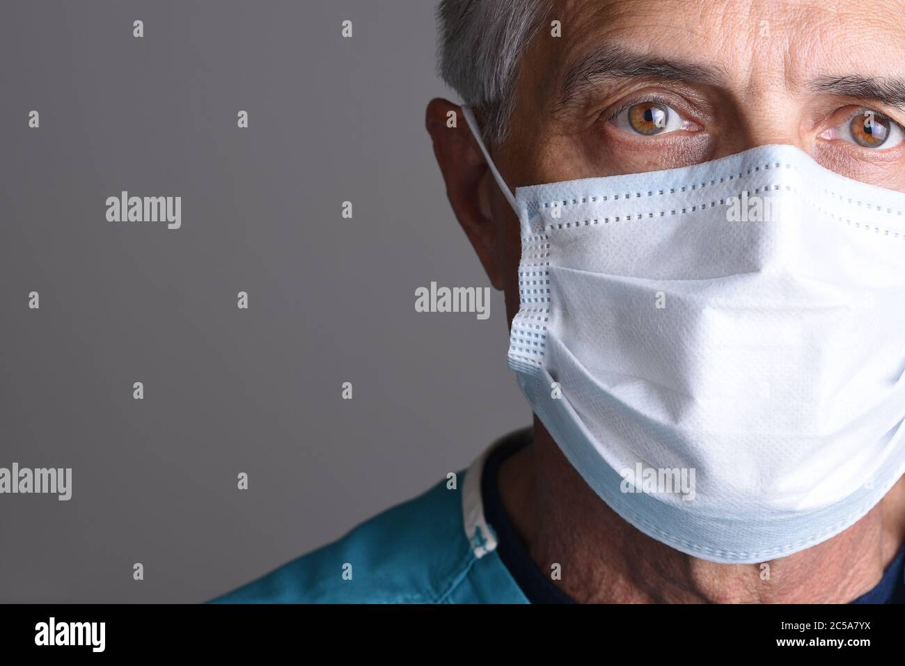Nahaufnahme Porträt eines reifen männlichen Arztes mit einer chirurgischen Maske. Es wird nur eine Teilfläche mit Kopierbereich auf einem grauen Hintergrund angezeigt. Stockfoto