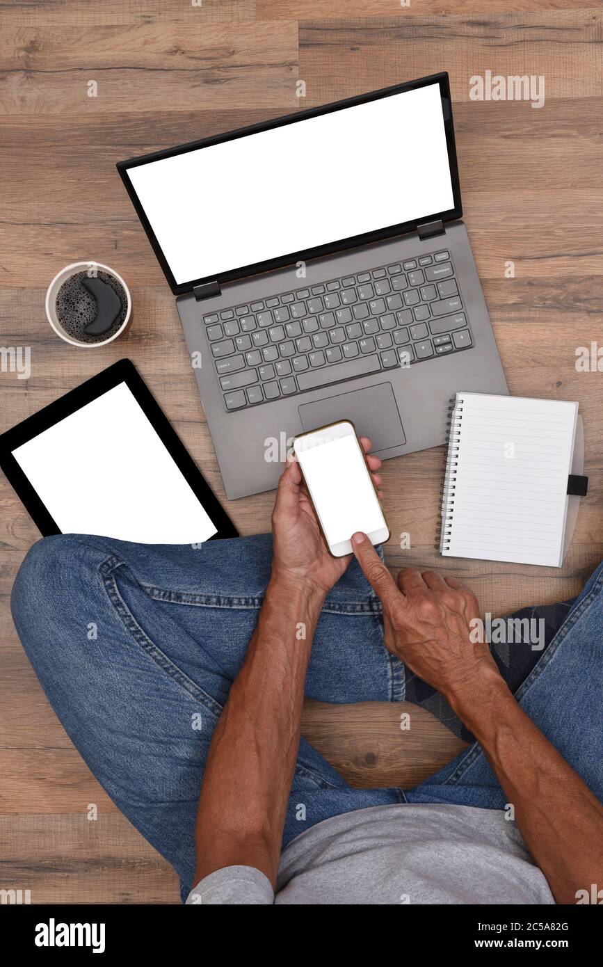 Hoher Winkel eines Mannes auf dem Boden mit seinen elektronischen Geräten sitzen - Smartphone, Laptop-Computer und Tablet mit weißen leeren Bildschirmen bereit für Ihre Stockfoto