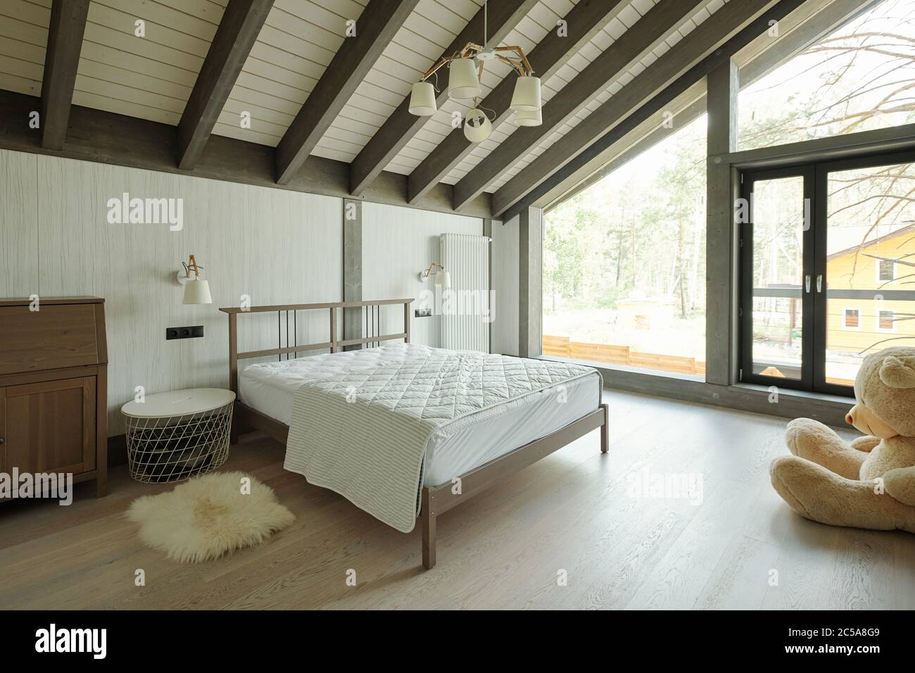 Gemütliches Schlafzimmer mit großen Spielzeugbär, kleiner Teppich Nachttisch und Doppelbett im Cottage House mit Glaswand Stockfoto