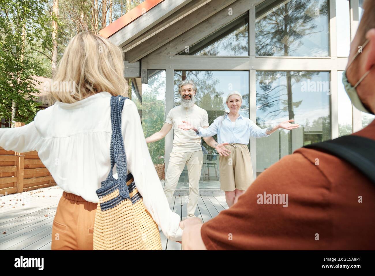 Glückliche ältere Eltern, die Arme für Umarmungen ausstreckten, während sie erwachsenen Sohn und Tochter im Cottage House begrüßten Stockfoto