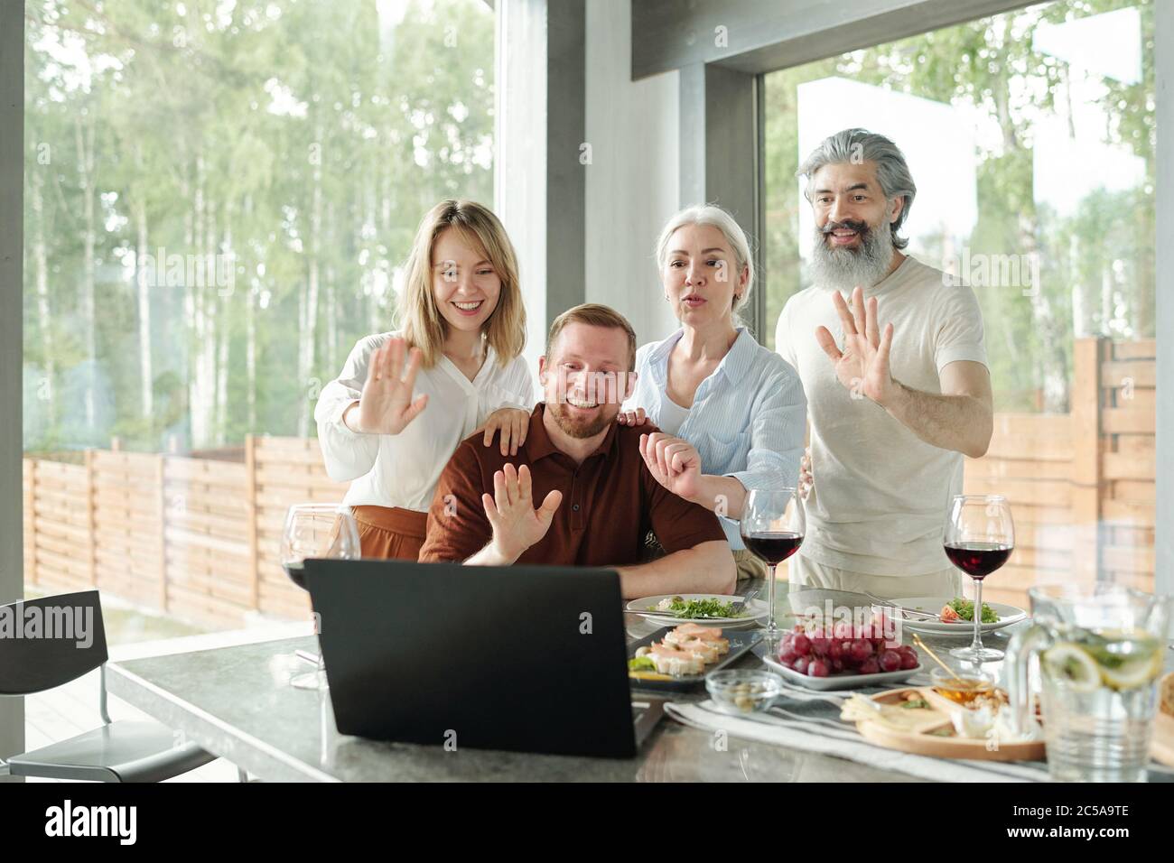 Ältere Eltern und ihre erwachsenen Kinder winken die Hände zum Laptop, während sie mit Verwandten über eine Videokonferenz-App sprechen Stockfoto