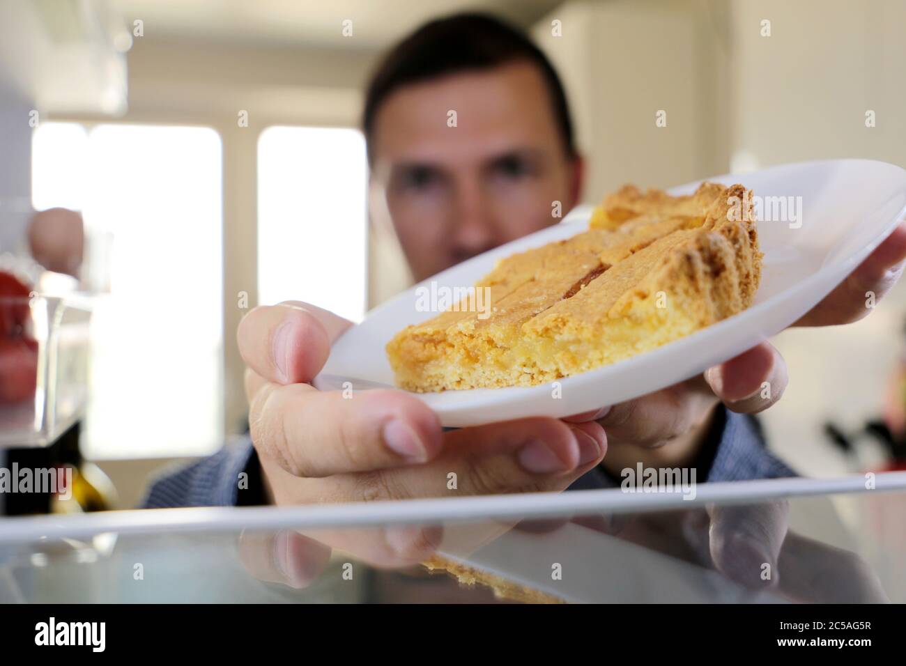 Der Mann nimmt eine Zitronenkuchen aus dem Kühlschrank. Konzept der Ernährung, Übergewicht und Süßigkeiten Stockfoto