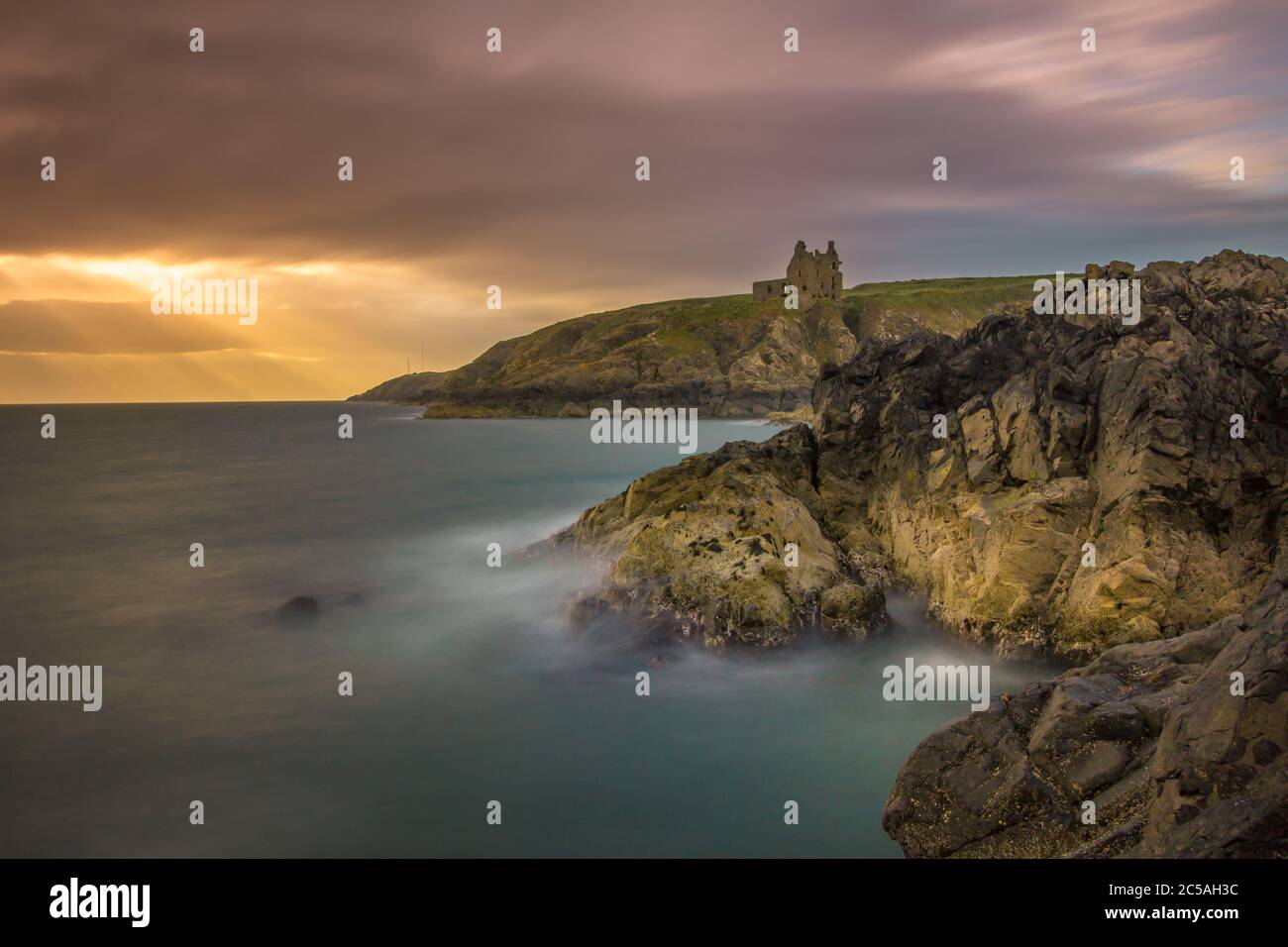 Lange Exposition der schottischen Küste mit Dunskey Castle im Hintergrund und Sonnenstrahlen auf den Klippen. Stockfoto