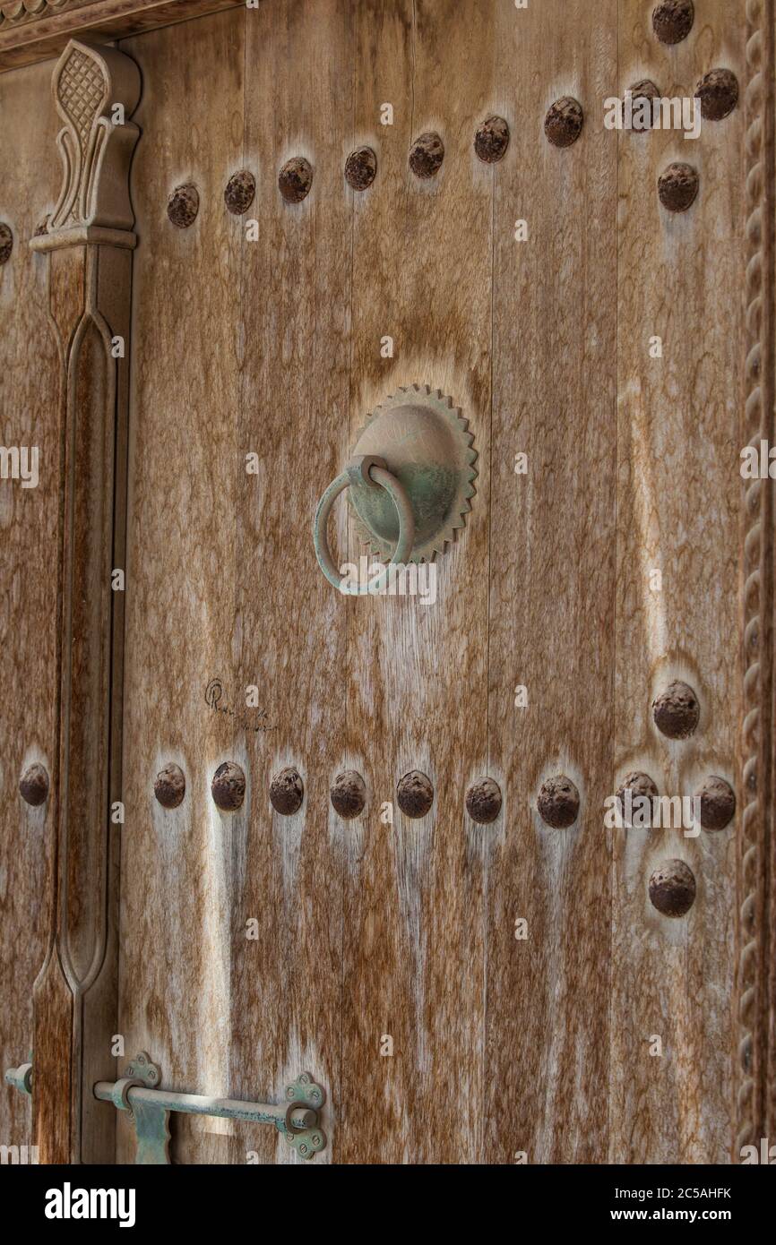 Verwitterte geschnitzte und verzierte Holztür Detail mit Metallgriffen. Katar. Stockfoto