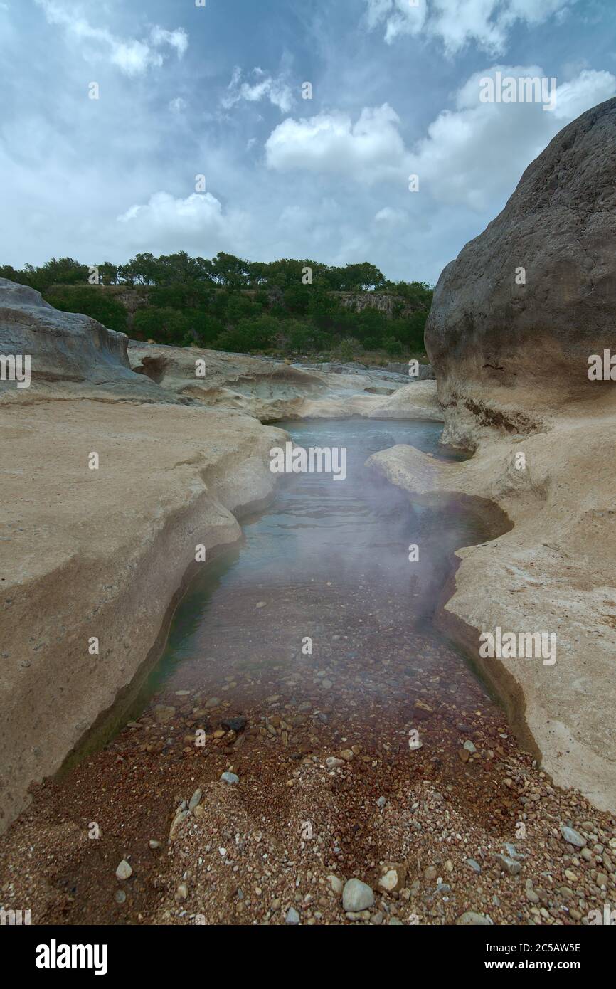 Nebel auf flachen Wasser Strand klar zeigt Felsen umgeben von Lärche Felsen Felsbrocken mit grünen Bäumen im Hintergrund Pedernales Falls State Park in Tex Stockfoto