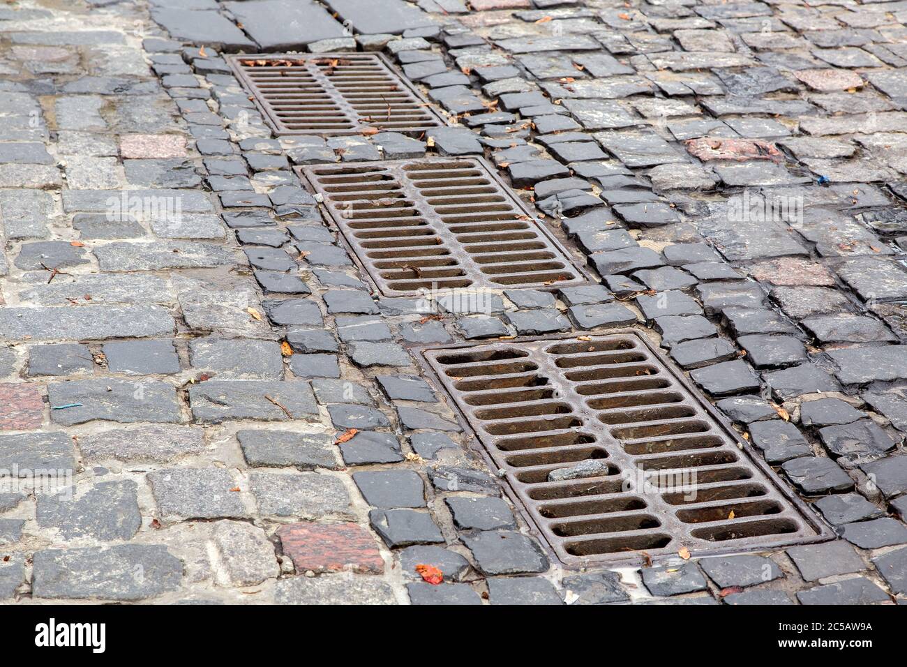 Hardscape sett Straße mit Eisenrost des Kanalisationssystems Luke auf dem Fußweg mit Pflastersteinen gepflastert, Nahaufnahme. Stockfoto