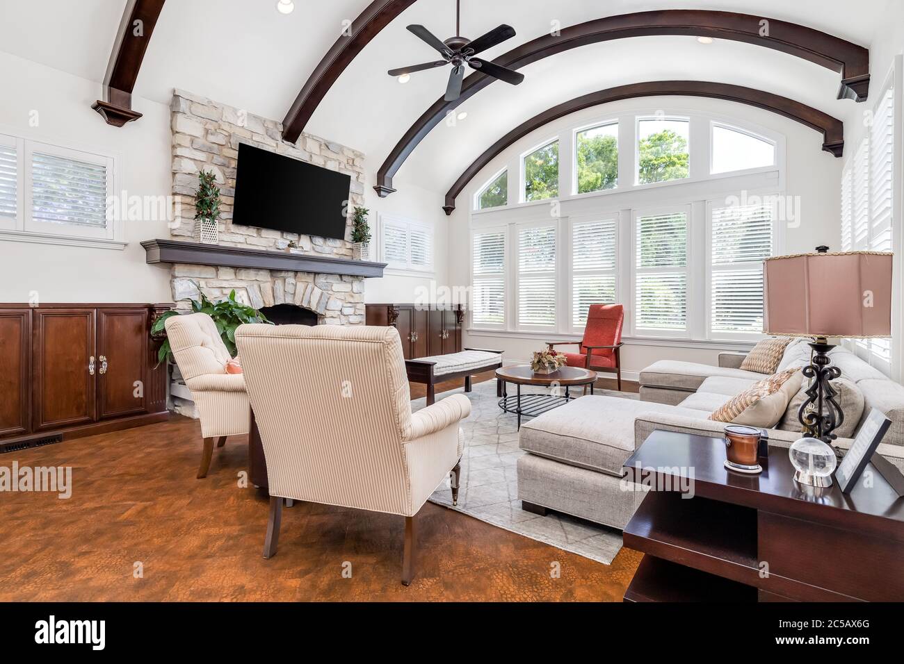Ein luxuriös eingerichtetes Wohnzimmer mit einem Fernseher, der auf einem Steinkamin montiert ist, Kupferböden und freiliegenden Holzbalken über der hohen Decke. Stockfoto