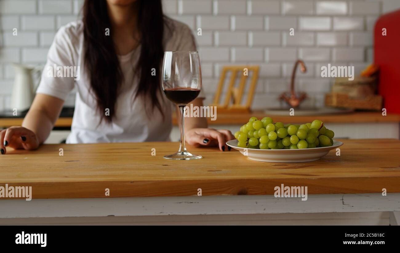 Junge Frau, die Trauben isst, am Tisch in der Küche sitzt. Nahaufnahme der Hand der Frau nimmt die Beere vom Teller. Stockfoto