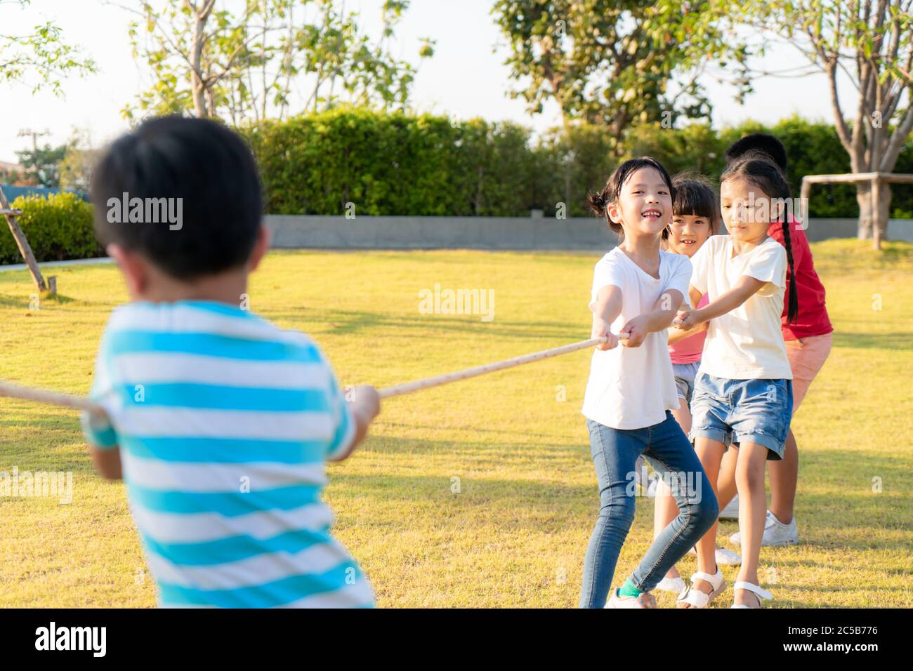 Gruppe glücklicher asiatischer Kleinkinder, die im Sommer auf dem Spielplatz im Stadtpark Krieg spielen oder Seiltogerther nach draußen ziehen. Kinder und Freizeit c Stockfoto