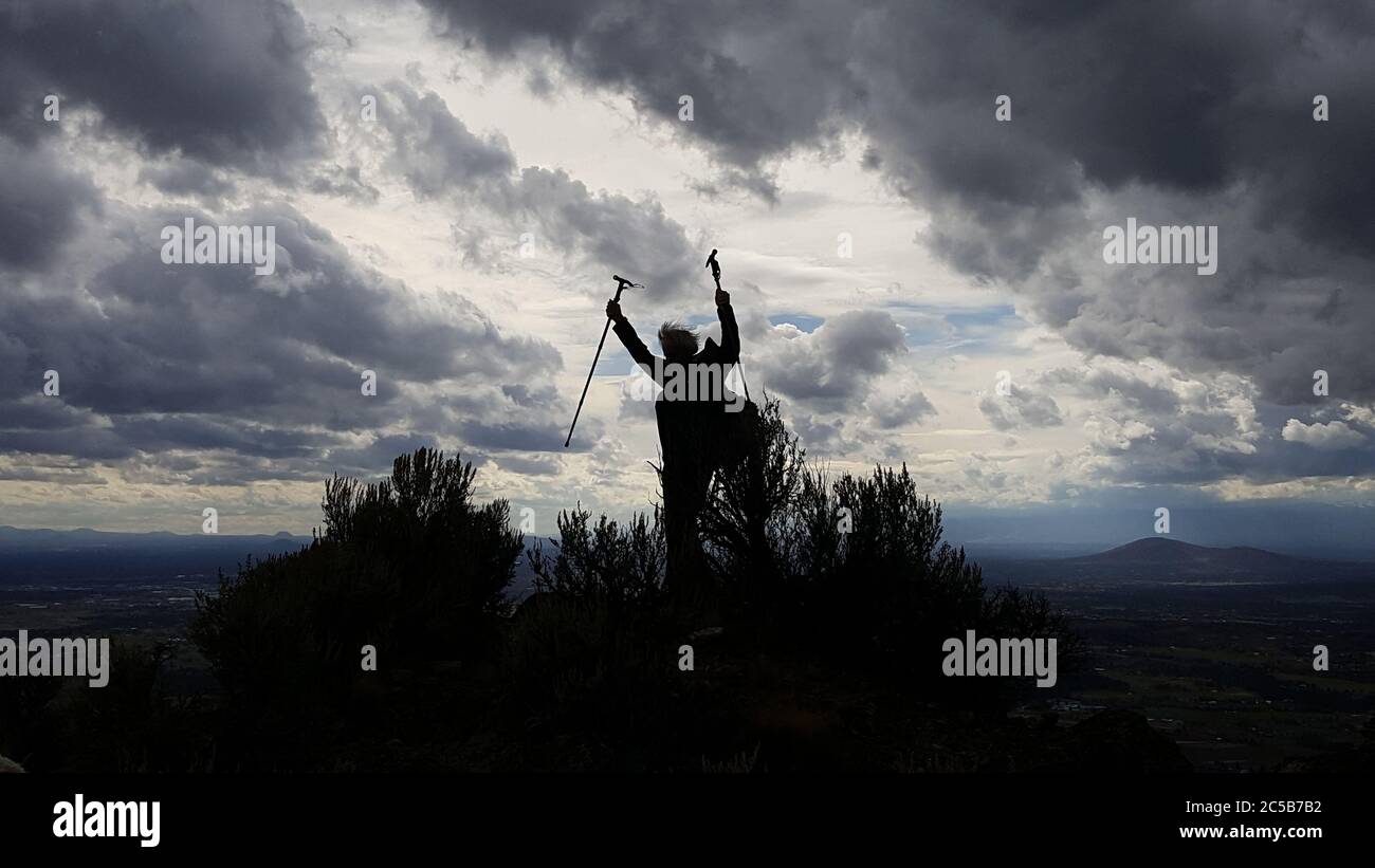 Die Silhouette eines männlichen Wanderers, der den Gipfel feiert, während ein Sturm hereinzieht. Stockfoto