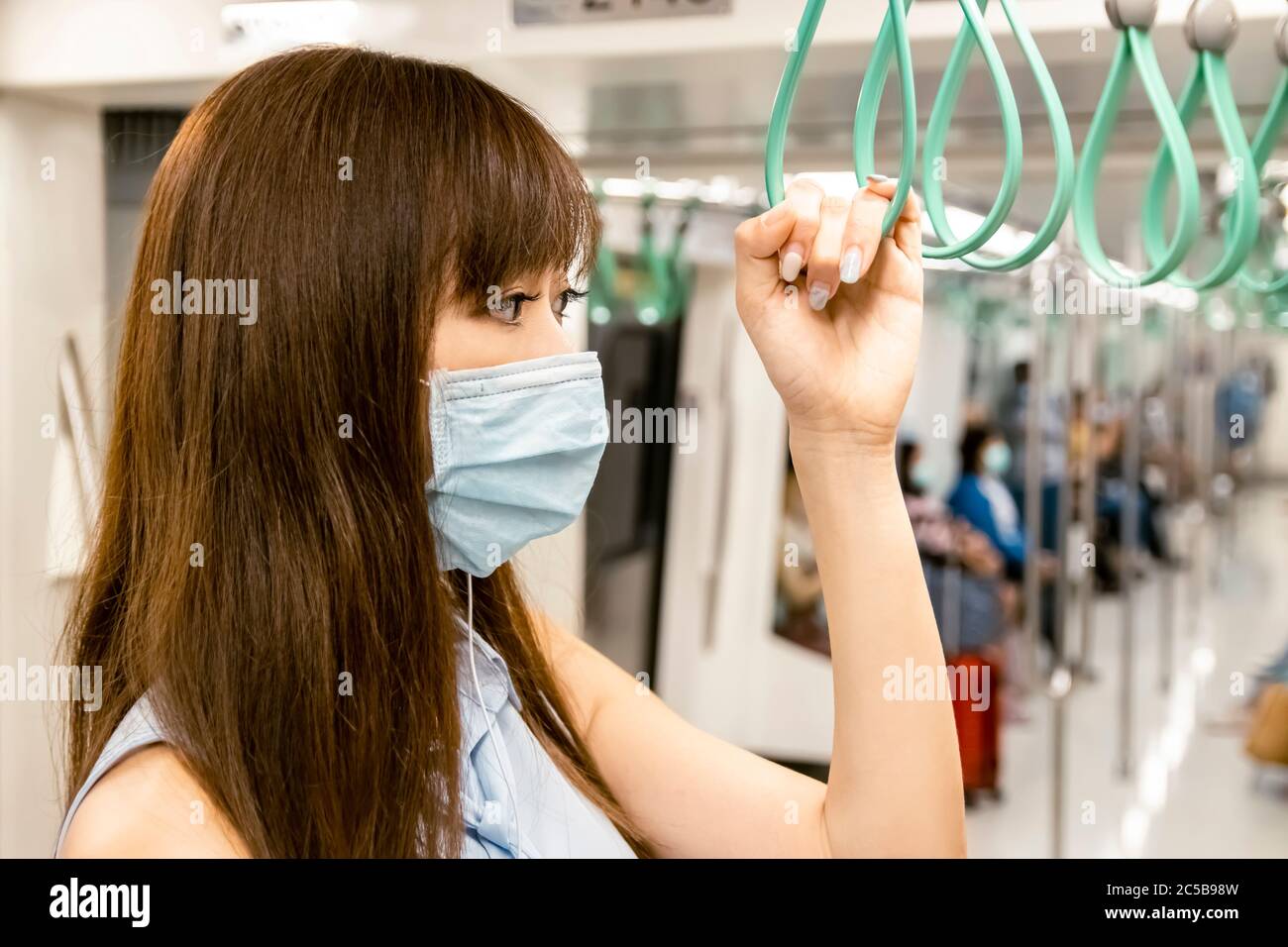 Junge asiatische Frau Passagier trägt chirurgische Maske und Musik hören über Handy in U-Bahn-Zug Stockfoto