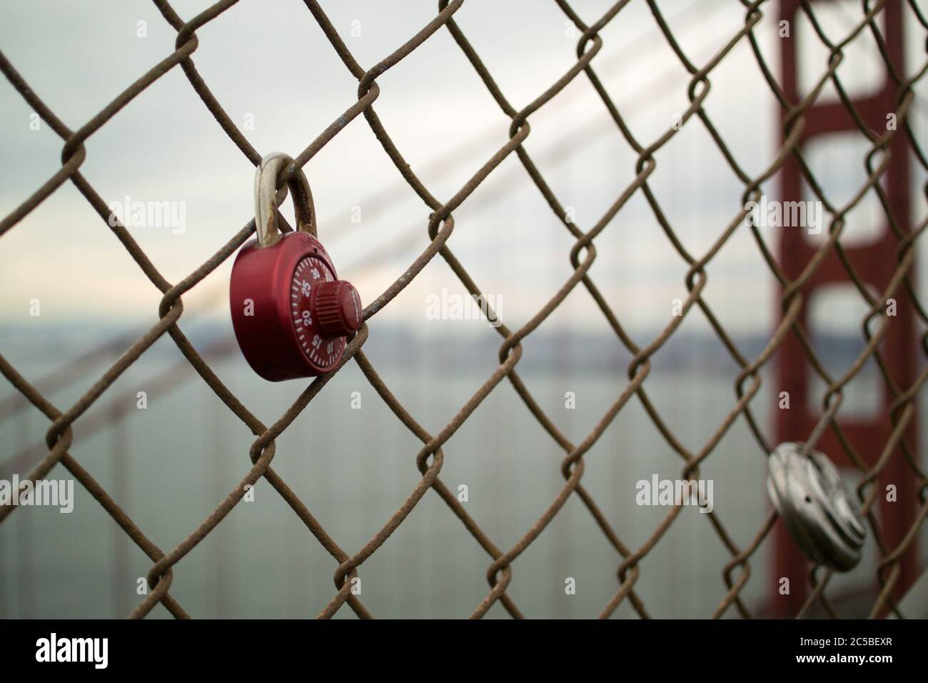 Liebesschlösser auf der Golden Gate Bridge, San Francisco, Kalifornien. Rotes Zahlenschloss und rundes Vorhängeschloss. Nördlicher Turm der ikonischen Brücke im Hintergrund. Stockfoto