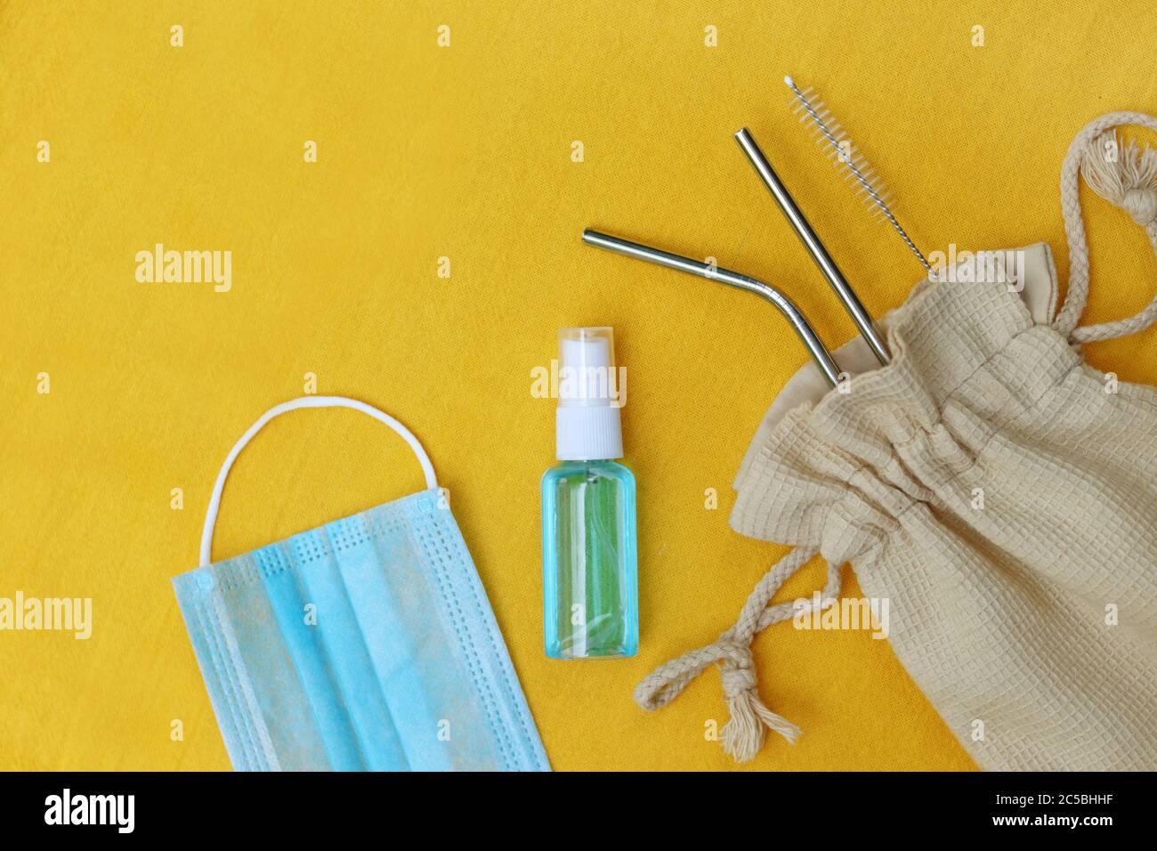 Medizinische Maske, Handdesinfektionsspray und wiederverwendbare Trinkhalme auf gelbem Hintergrund. Konzept für neuen normalen oder neuen Lebensstil nach COVID-19. Stockfoto