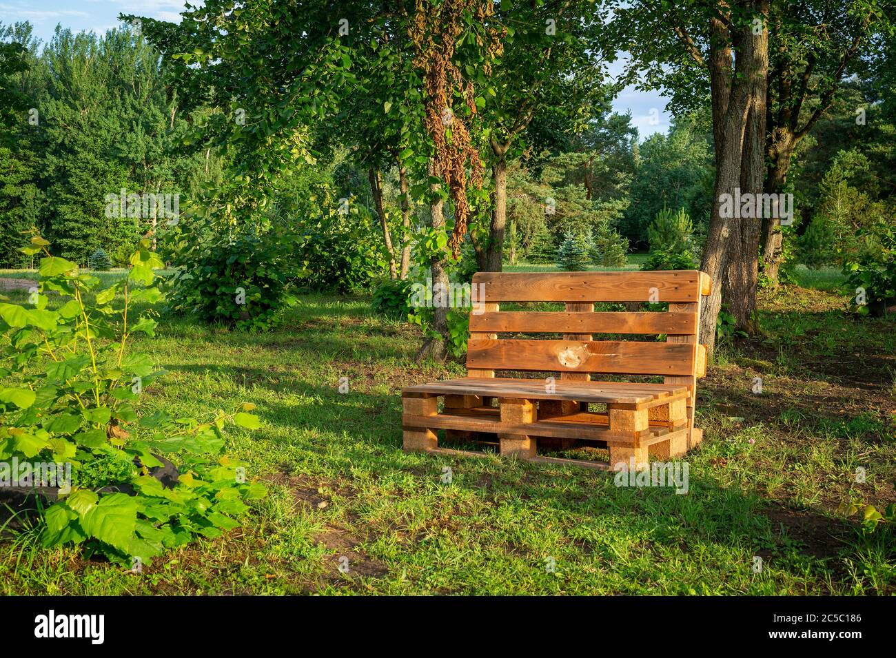 Gartenmöbel aus Holzpaletten, umgeben von Bäumen und Grün in der Sommersonne Stockfoto