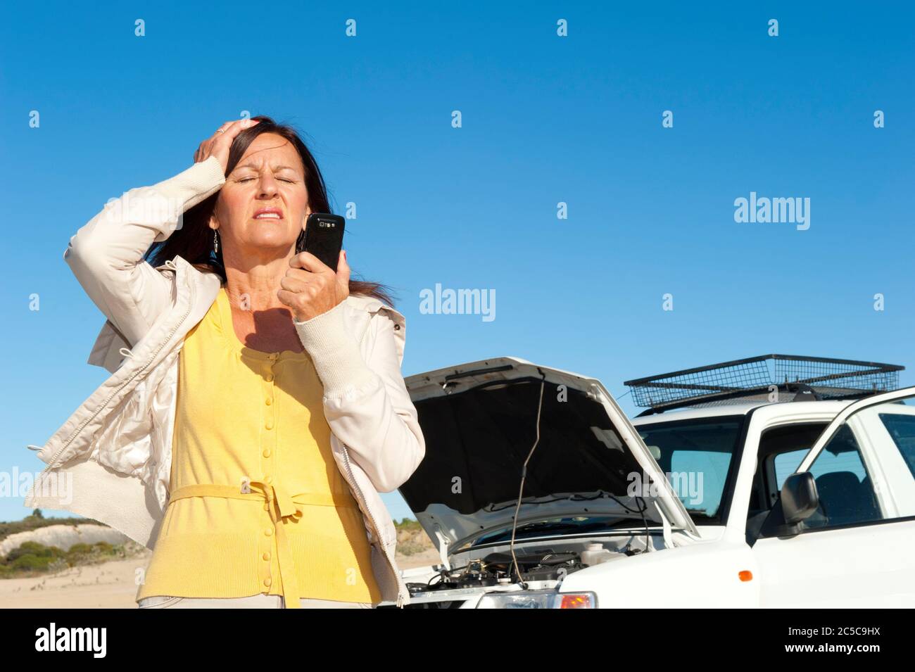 Gestresste reife Frau Zusammenbruch mit Auto auf abgelegene Straße rufen um Hilfe, für Hilfe auf Handy, isoliert mit blauen Himmel als Hintergrund und Polizist Stockfoto