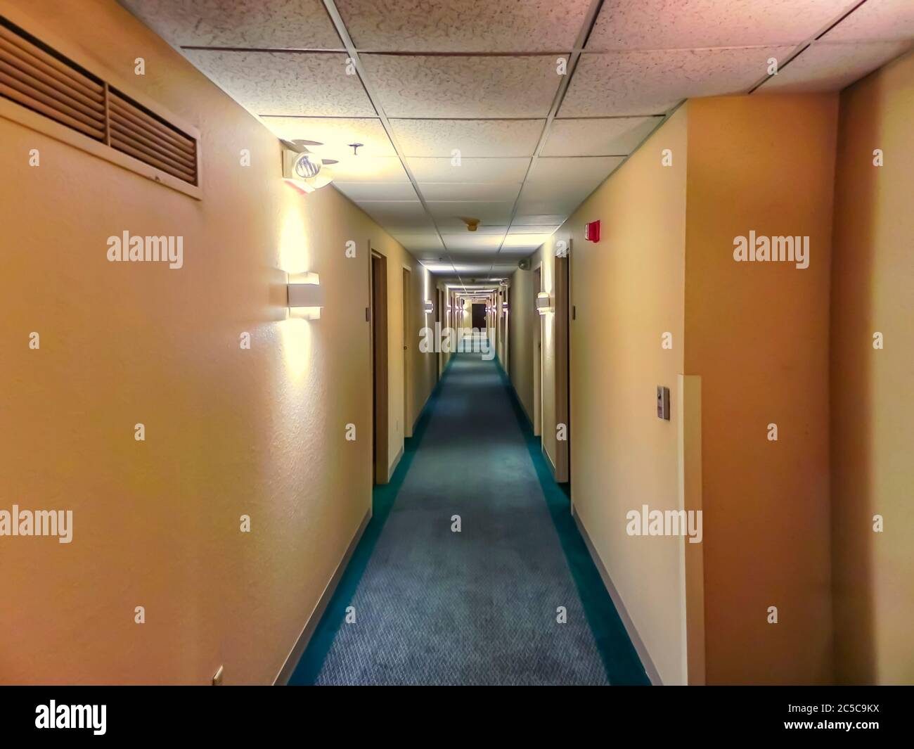 Blick auf den langen Hotelkorridor, beleuchtet von einer Reihe von Lichtern. Im Bild sind Eingänge zu den Räumen sichtbar. Stockfoto