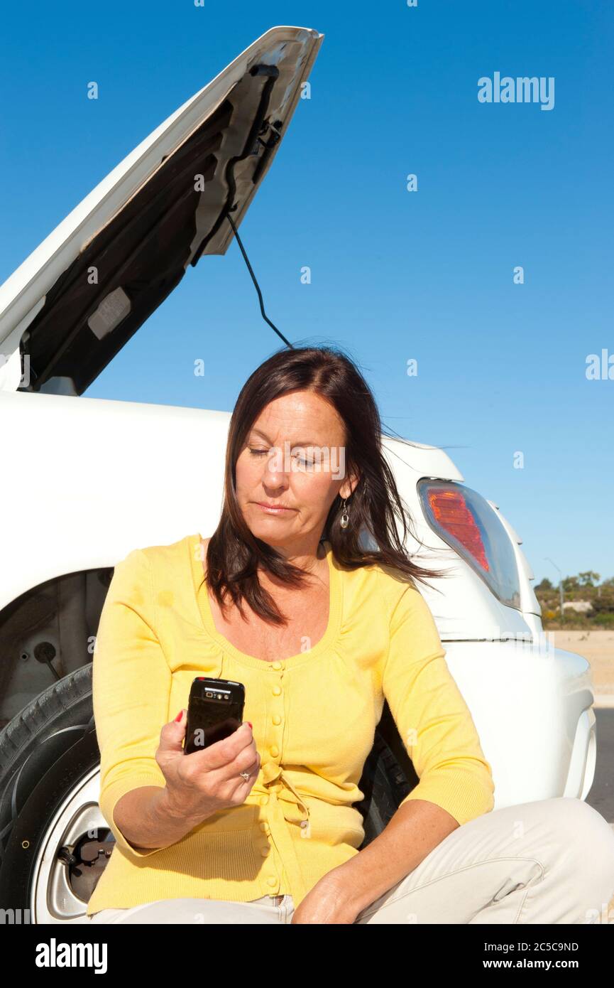 Gestresste reife Frau Zusammenbruch mit Auto auf abgelegene Straße rufen um Hilfe, für Hilfe auf Handy, isoliert mit blauen Himmel als Hintergrund und Polizist Stockfoto