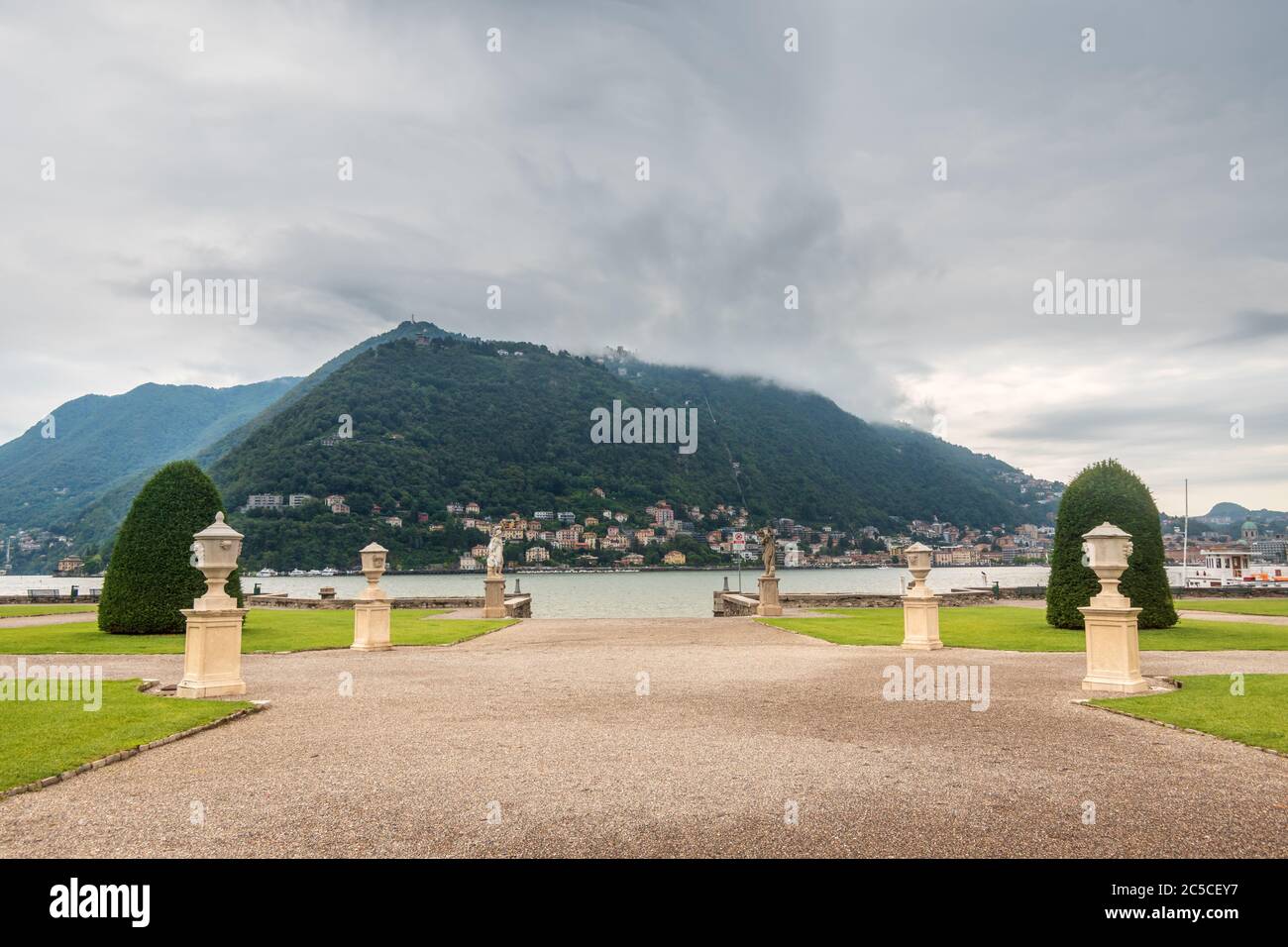 Malerische Allee mit Skulpturen in einem Sommergarten, der zum Comer See führt, einem hohen Berg, der mit Wolken im Hintergrund bedeckt ist, Villa Olmo, Italien. Stockfoto