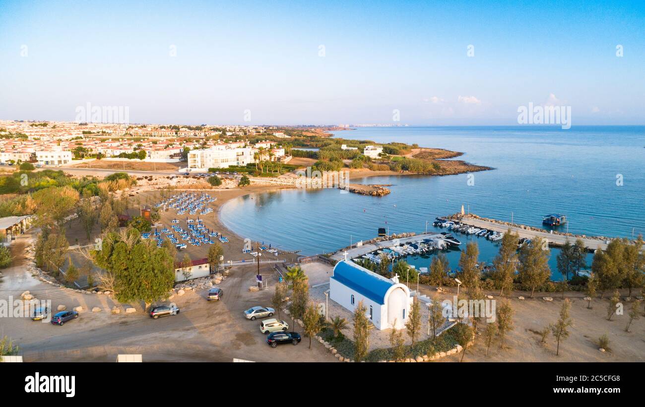 Luftbild des Sonnenuntergangs an der Küste und die weiße, gewaschene Kapelle am Strand Agia Triada, Protaras, Famagusta, Zypern von oben. Vogelperspektive auf Tour Stockfoto