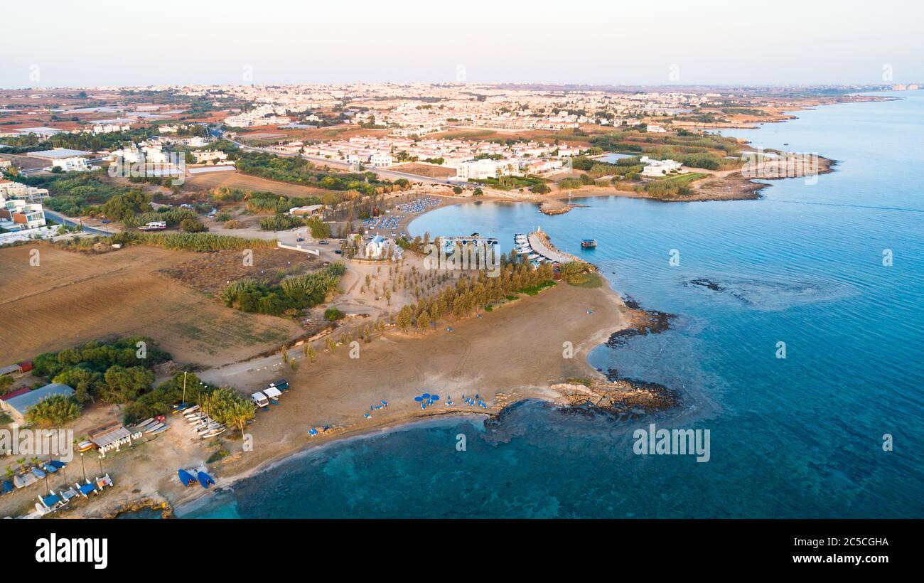 Luftbild des Sonnenuntergangs an der Küste und die weiße, gewaschene Kapelle am Strand Agia Triada, Protaras, Famagusta, Zypern von oben. Vogelperspektive auf Tour Stockfoto