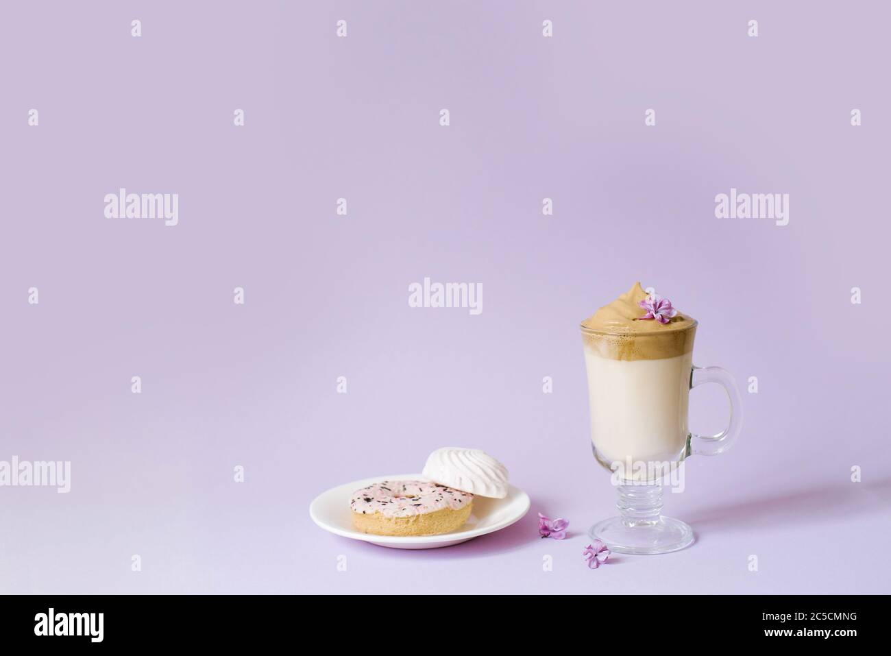 Schöne dalgona trinken einen schaumigen Kaffee in einem transparenten Becher und Blumen lila Il lila Hintergrund. Süßigkeiten auf einem Teller: Donat und zartes mar Stockfoto