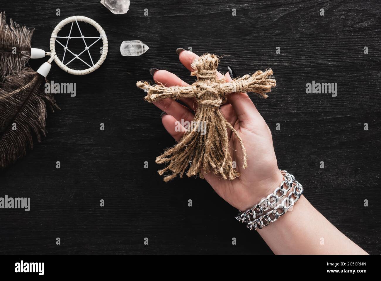 Draufsicht auf Frau, die Voodoo Puppe in der Nähe von Pentagramm und Kristallen auf schwarz hält Stockfoto